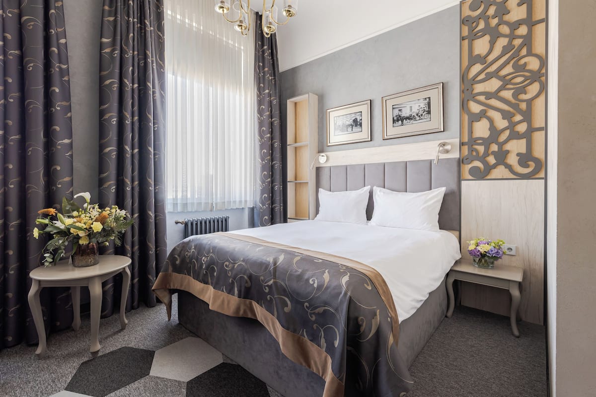 A hotel room with a large bed, a bedside table with a vase of flowers, a nightstand with a vase, and a decorative wall panel.