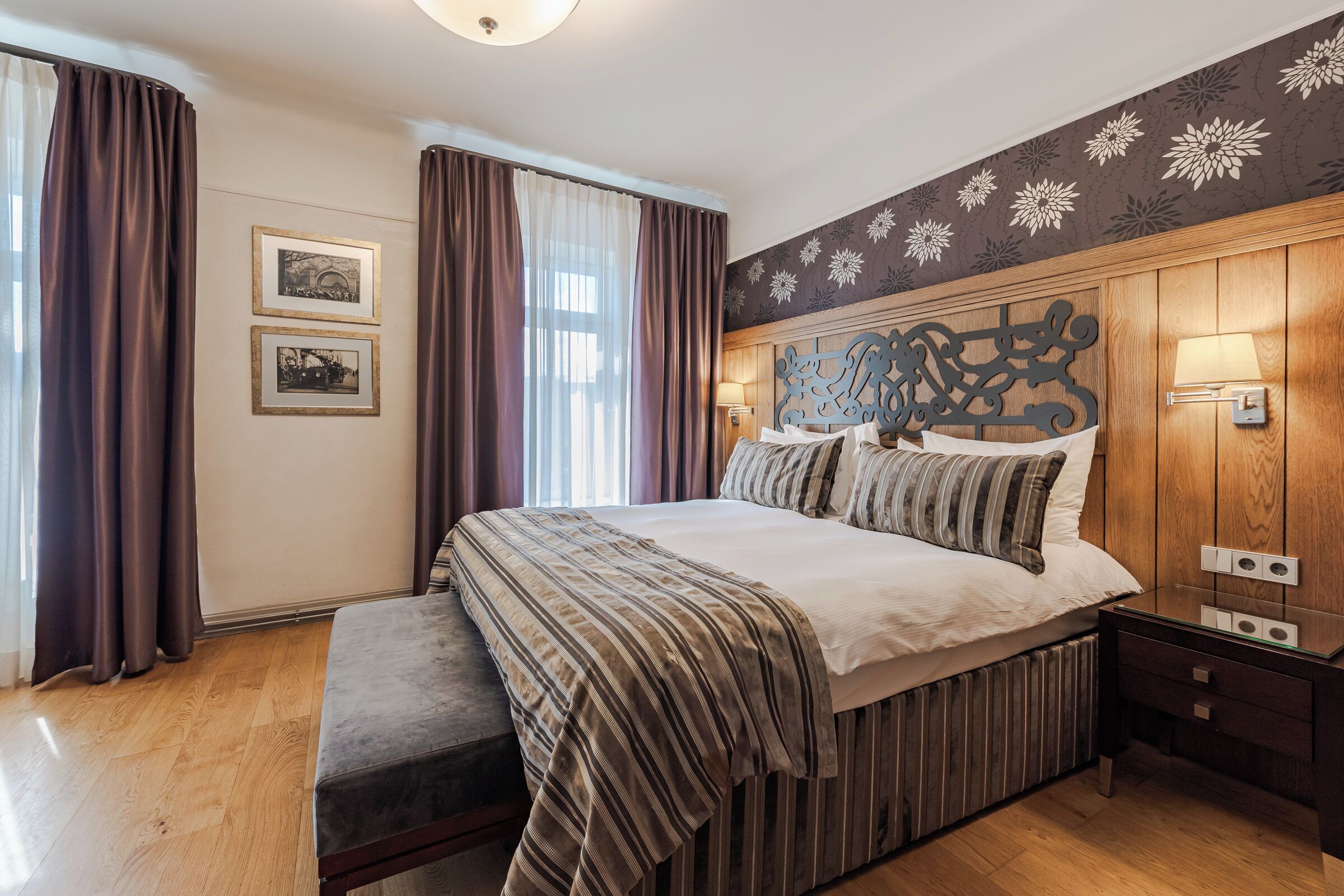 A bedroom with a large bed, wooden headboard, two wall-mounted lamps, and a bench.