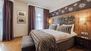 A bedroom with a large bed, wooden headboard, two wall-mounted lamps, and a bench.