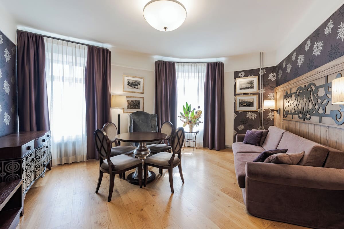 A modern living room with a dining area, featuring a round table, dark brown sofa, and a decorative wall piece.
