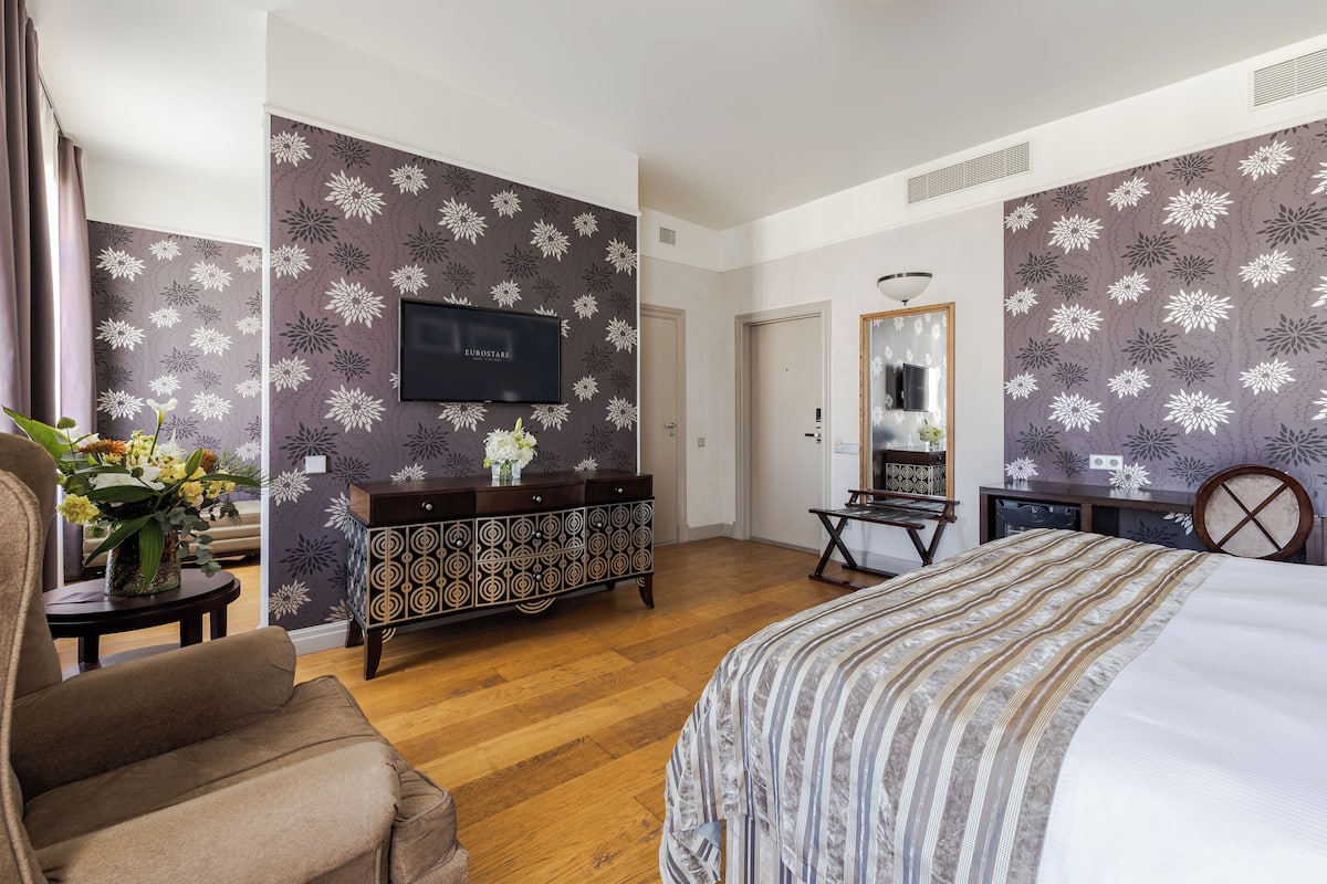 Hotellihuone, jossa on sänky, televisio, lipasto ja peili.