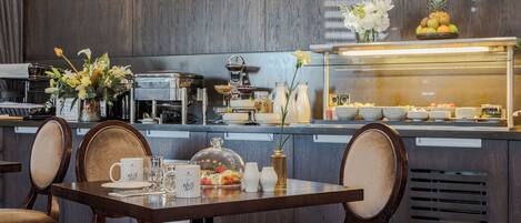 Un restaurante con interiores de madera, una barra de buffet con frutas y verduras, y un comedor con sillas y una mesa dispuesta para dos.