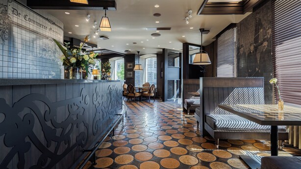 Un interior moderno con suelo estampado, una zona de bar con pared decorativa y un espacio de estar con mesa y banco.