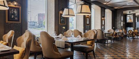 A restaurant with a modern interior, featuring a patterned floor, multiple dining tables, and chairs.