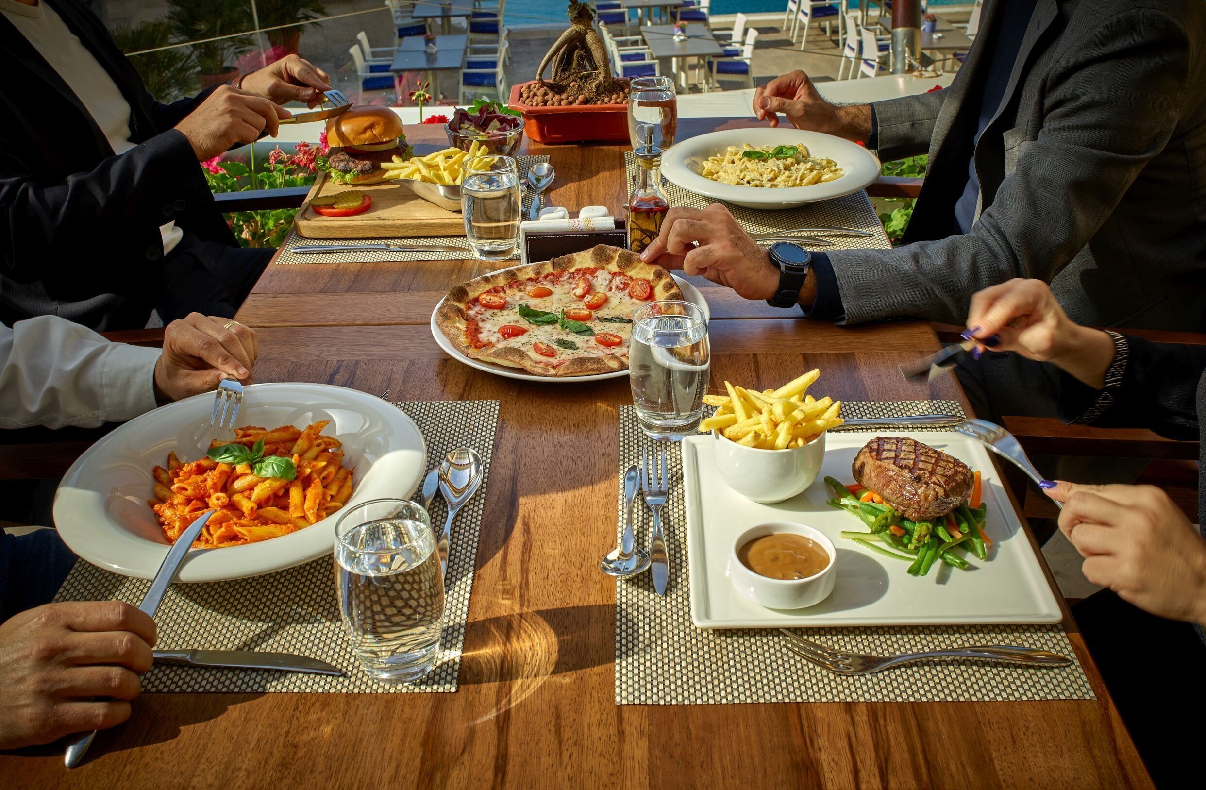 Un tavolo da pranzo con diversi piatti, tra cui pasta, pizza, patatine fritte e una bistecca con verdure.