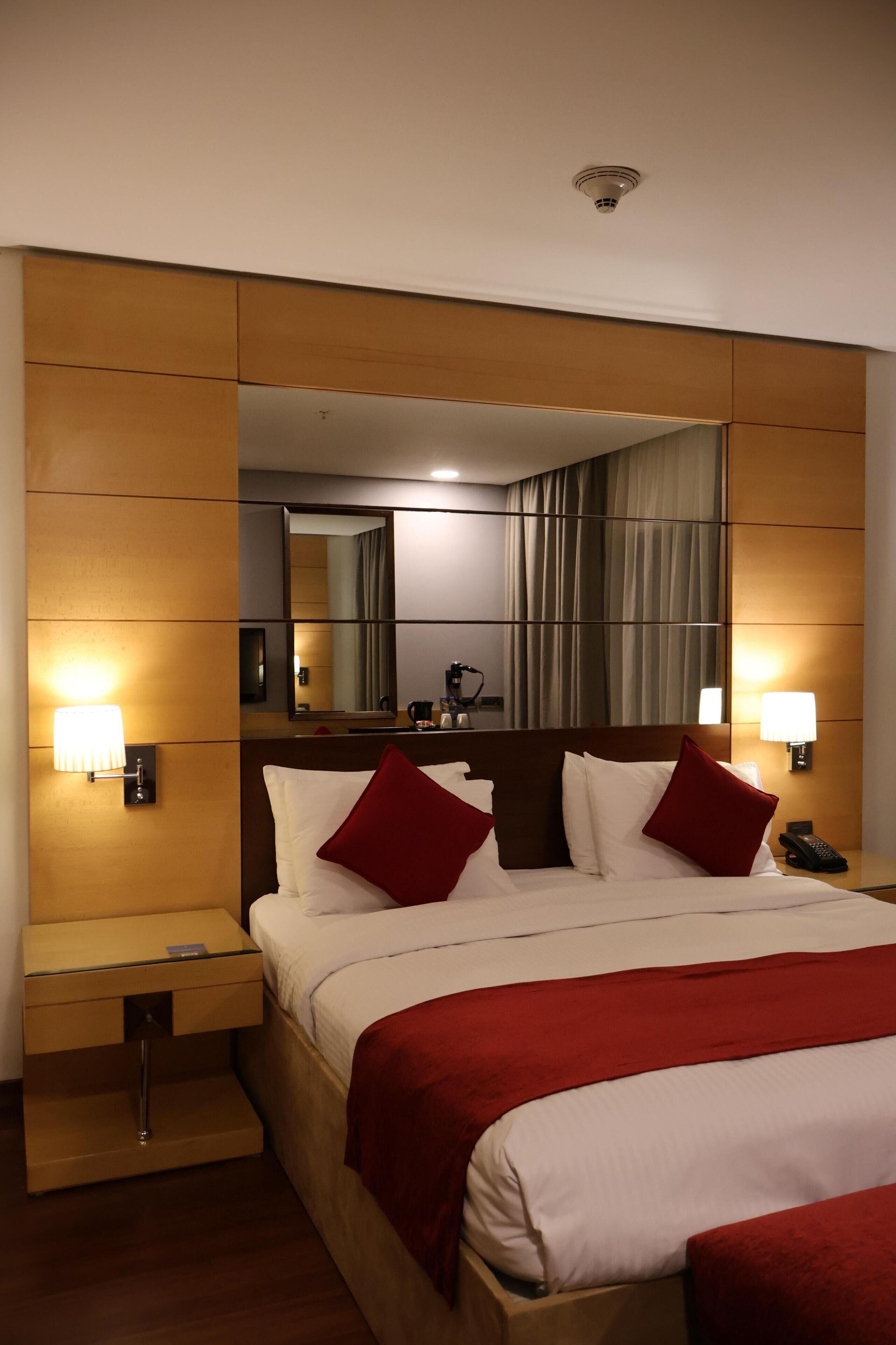 Une chambre d’hôtel avec un grand lit, deux tables de chevet, une commode, un miroir et une lampe fixée au mur.