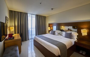Habitación de hotel con una cama grande, mesitas de noche, televisión, escritorio y ventana con cortinas.