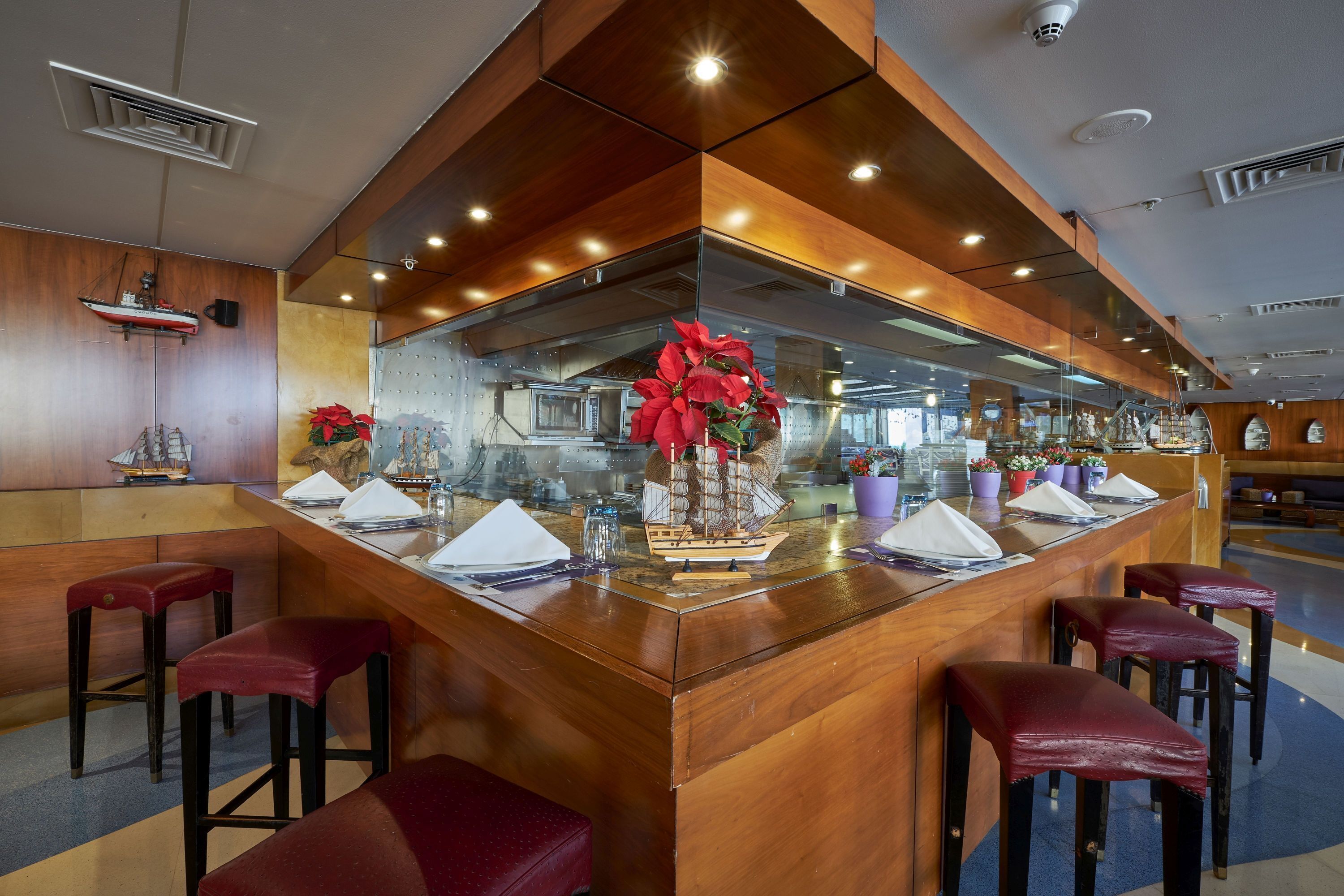 A bar area with wooden bar stools, a ship model, and a large red flower centerpiece.