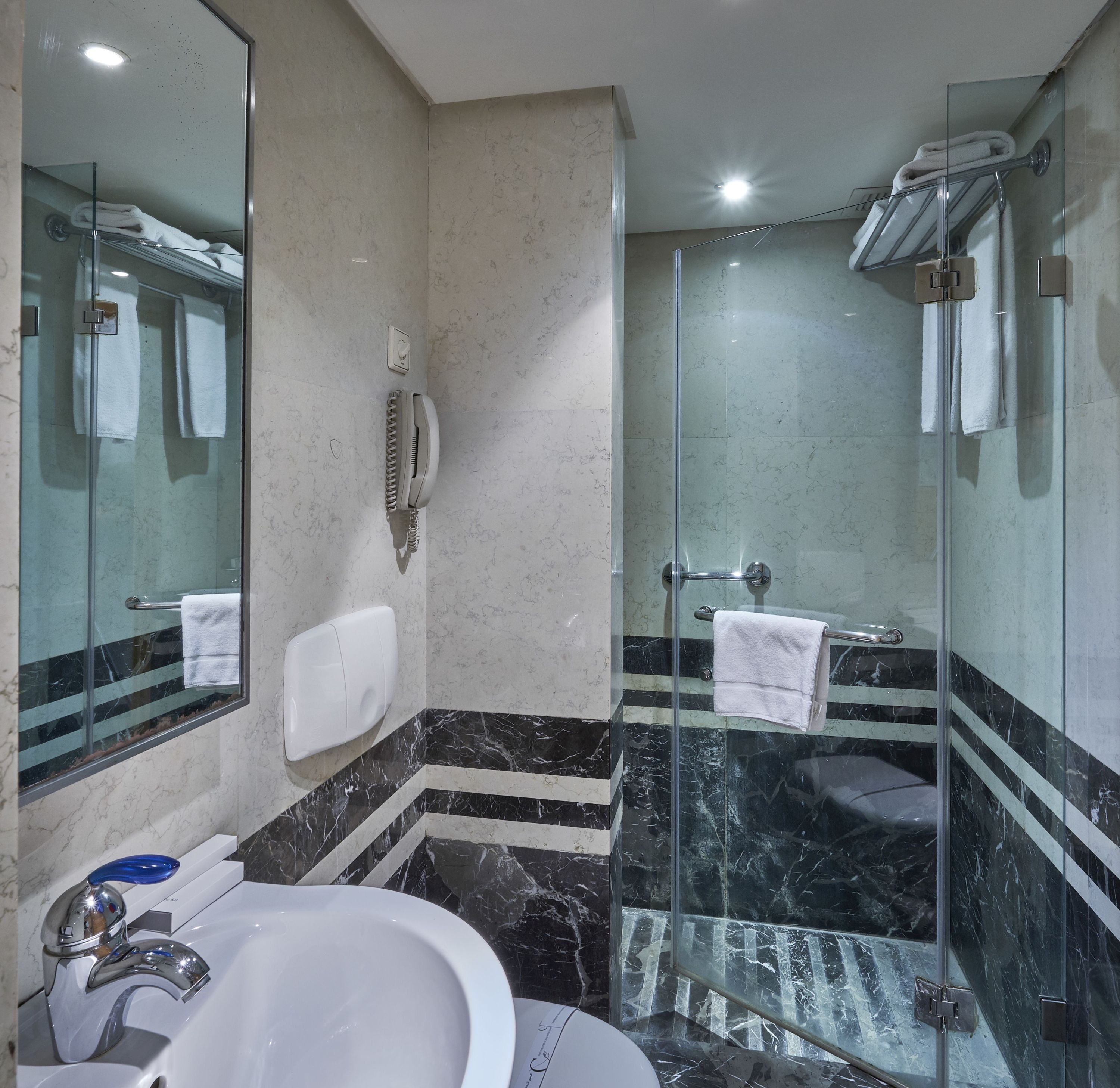 Un baño moderno con ducha de vidrio, un lavabo blanco y suelo de mármol.