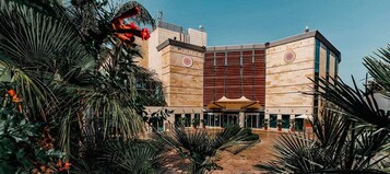 Un edificio moderno con un atrio central, rodeado de palmeras y zonas de estar al aire libre.