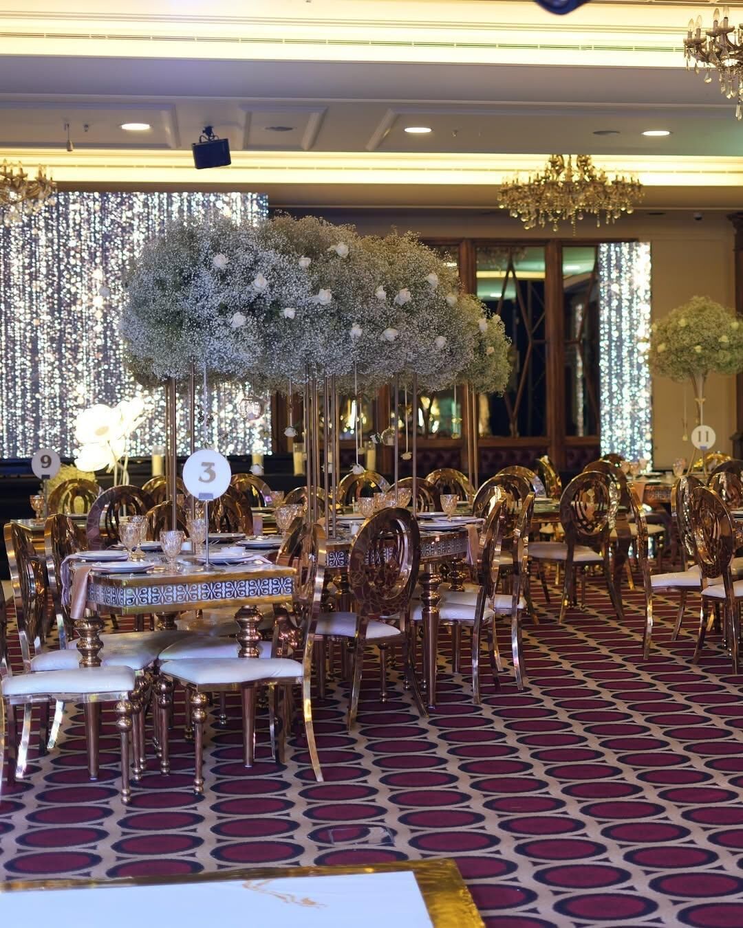 A banquet hall with round tables, chairs, and a decorative floral arrangement.