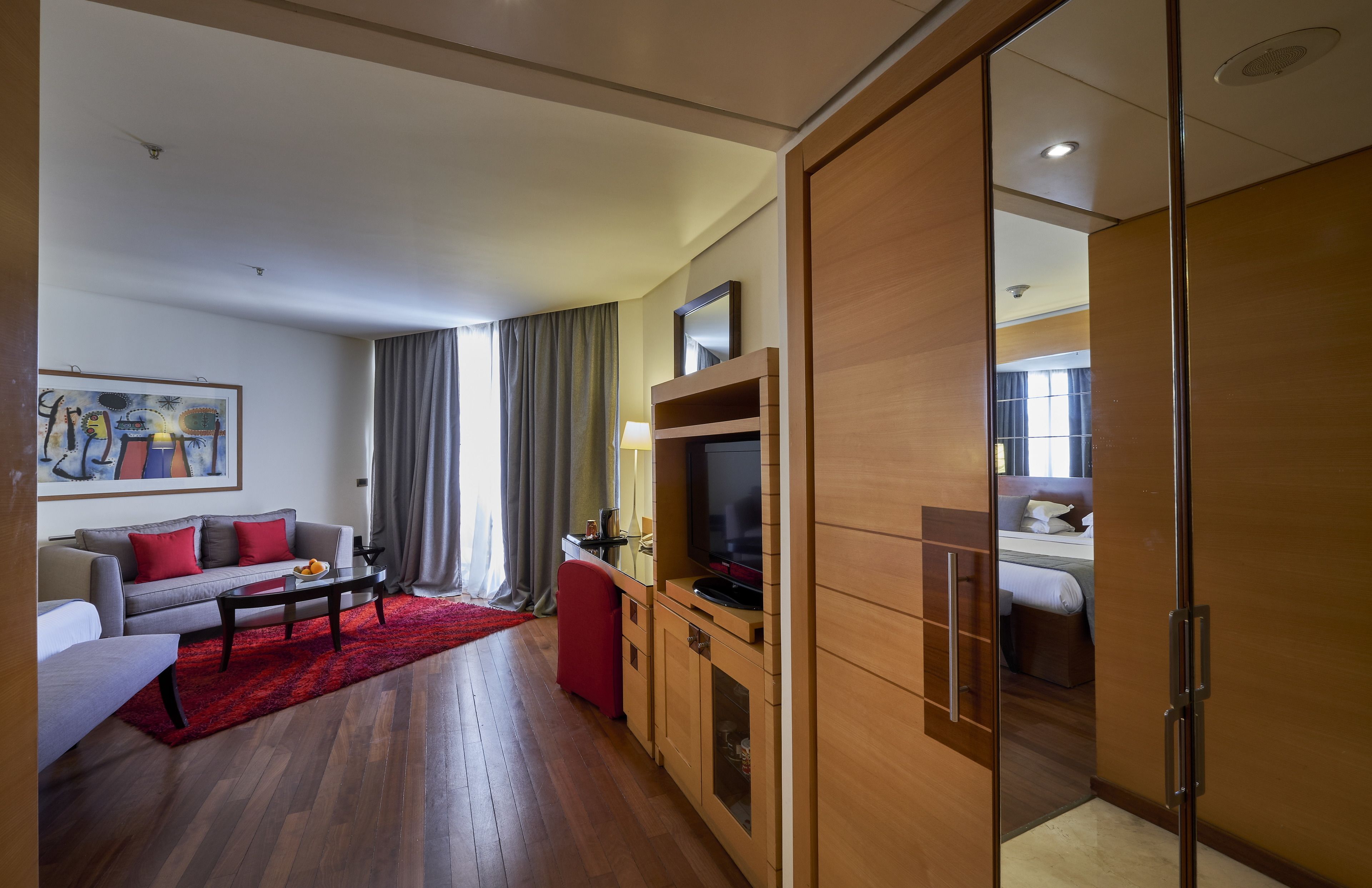 A modern hotel room with a sofa, a TV, a red rug, and a wooden cabinet.