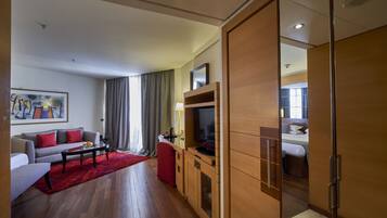 A modern hotel room with a sofa, a TV, a red rug, and a wooden cabinet.