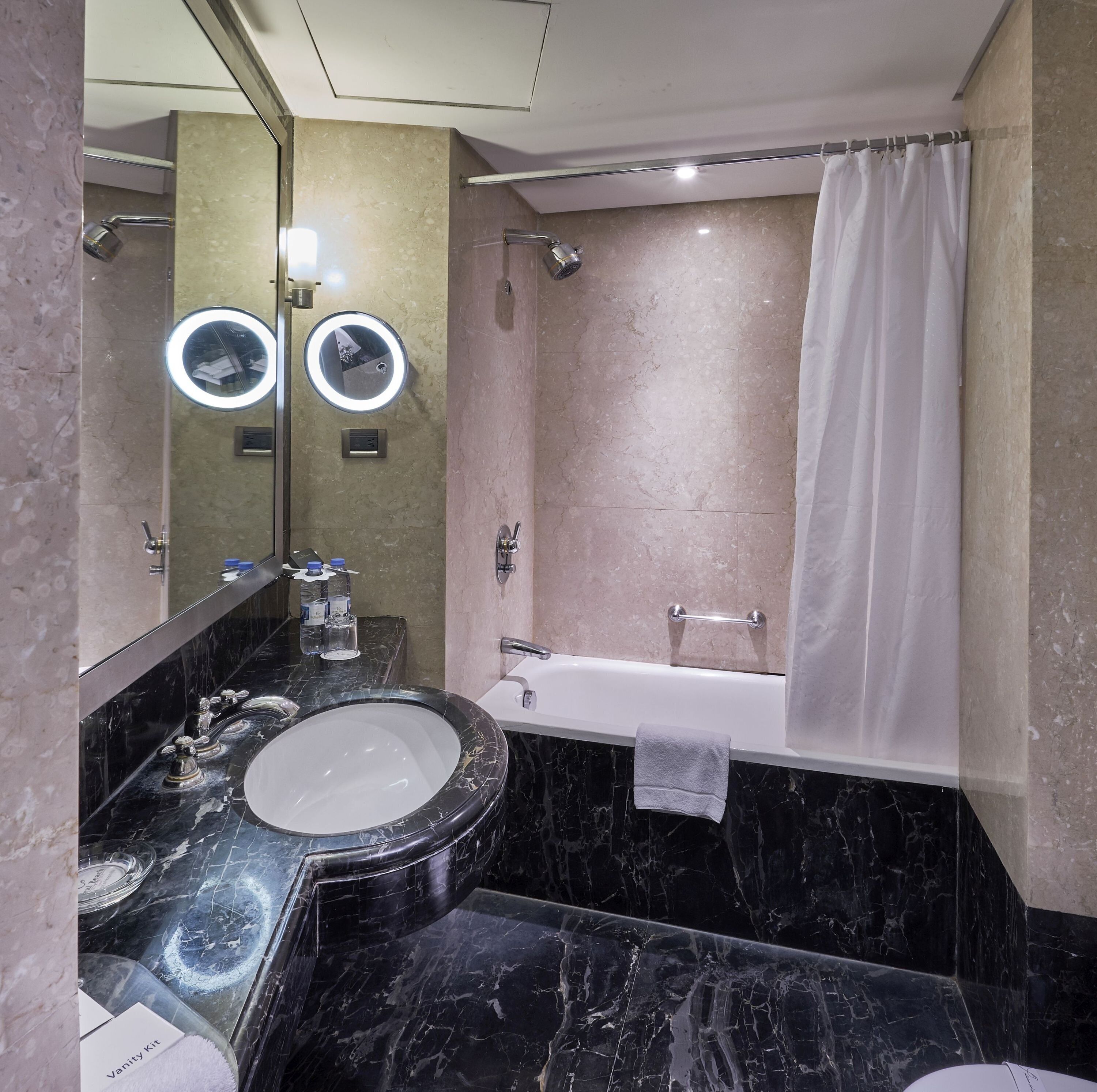 A bathroom with a marble sink, a bathtub, a shower, and a mirror with lights.