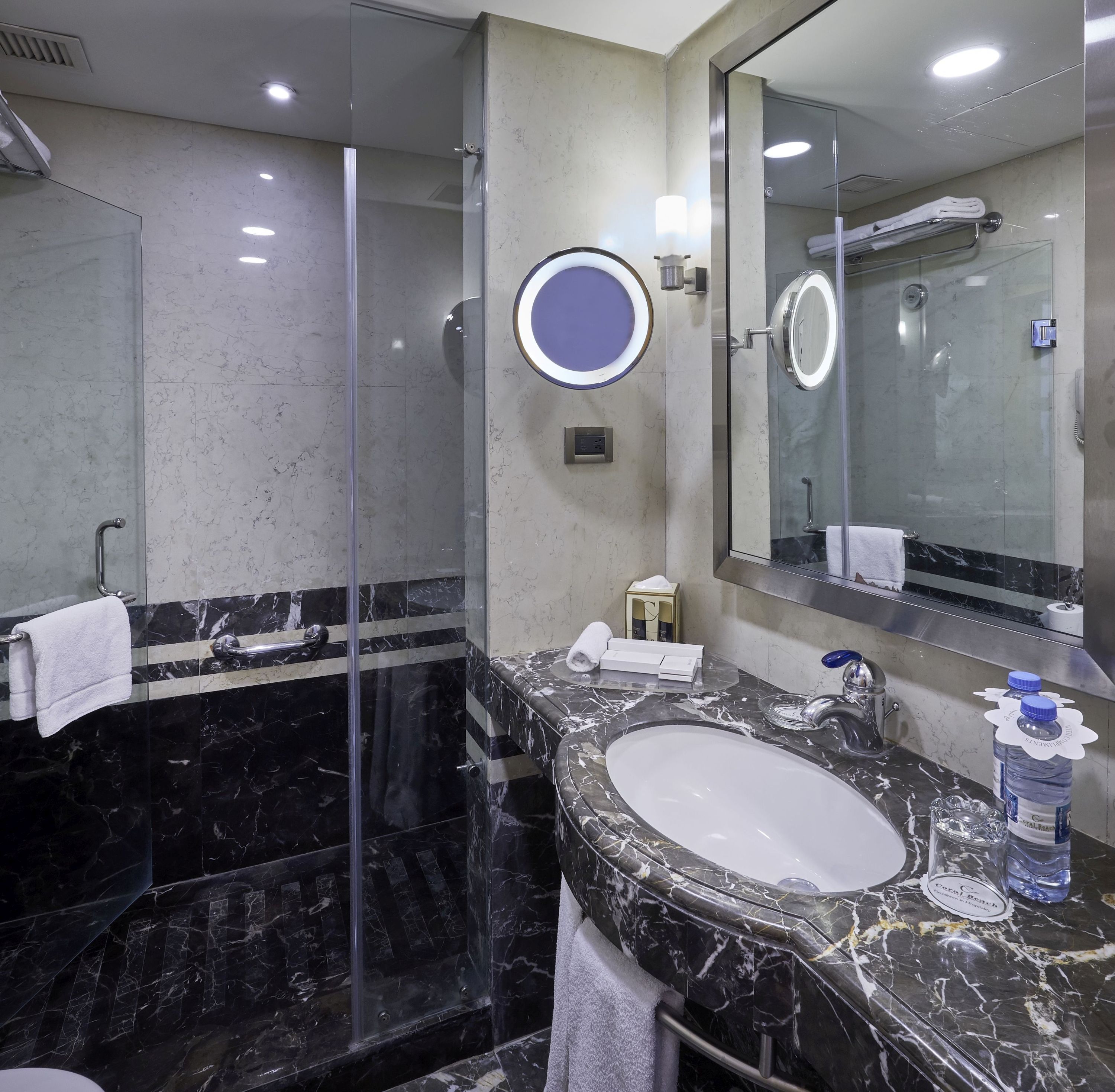 Un baño moderno con ducha acristalada, lavabo de mármol y un espejo grande.