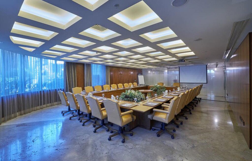 A conference room with a long table, chairs, a projector screen, and a large window with curtains.