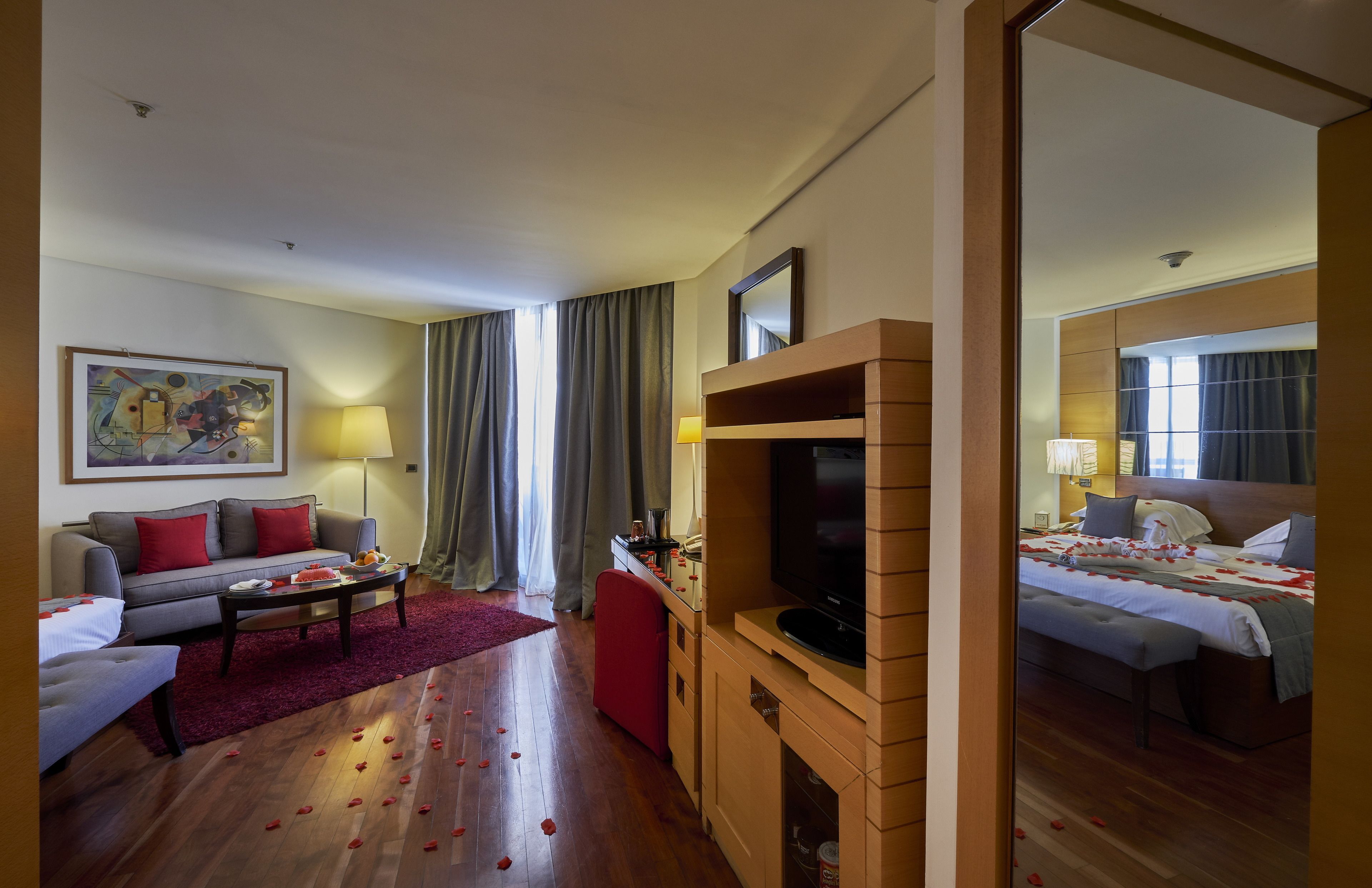 A hotel room with a sofa, a coffee table, a TV, a bed, and a red carpet.