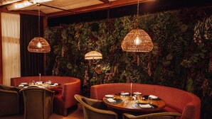 Ein Restaurant mit runden Tischen und rot gepolsterten Sitzbänken, mit einer Grünwand und hängenden Korbstühlen.