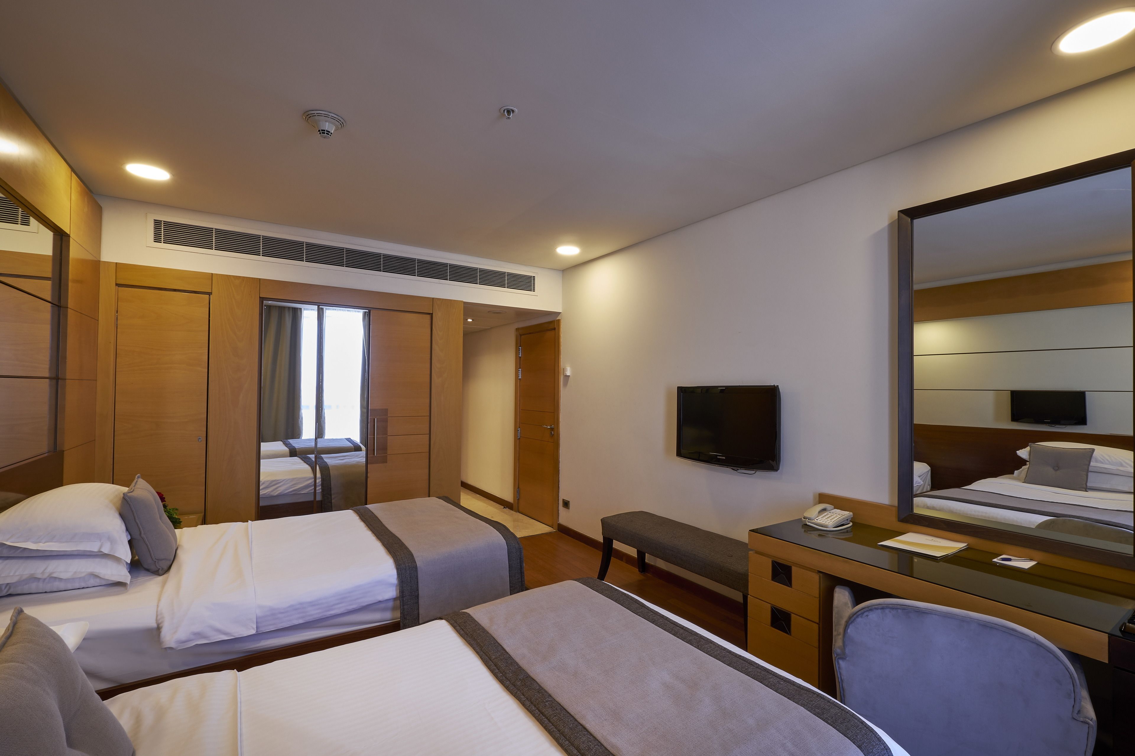 A hotel room with two beds, a desk with a telephone, a mirror, and a television on the wall.
