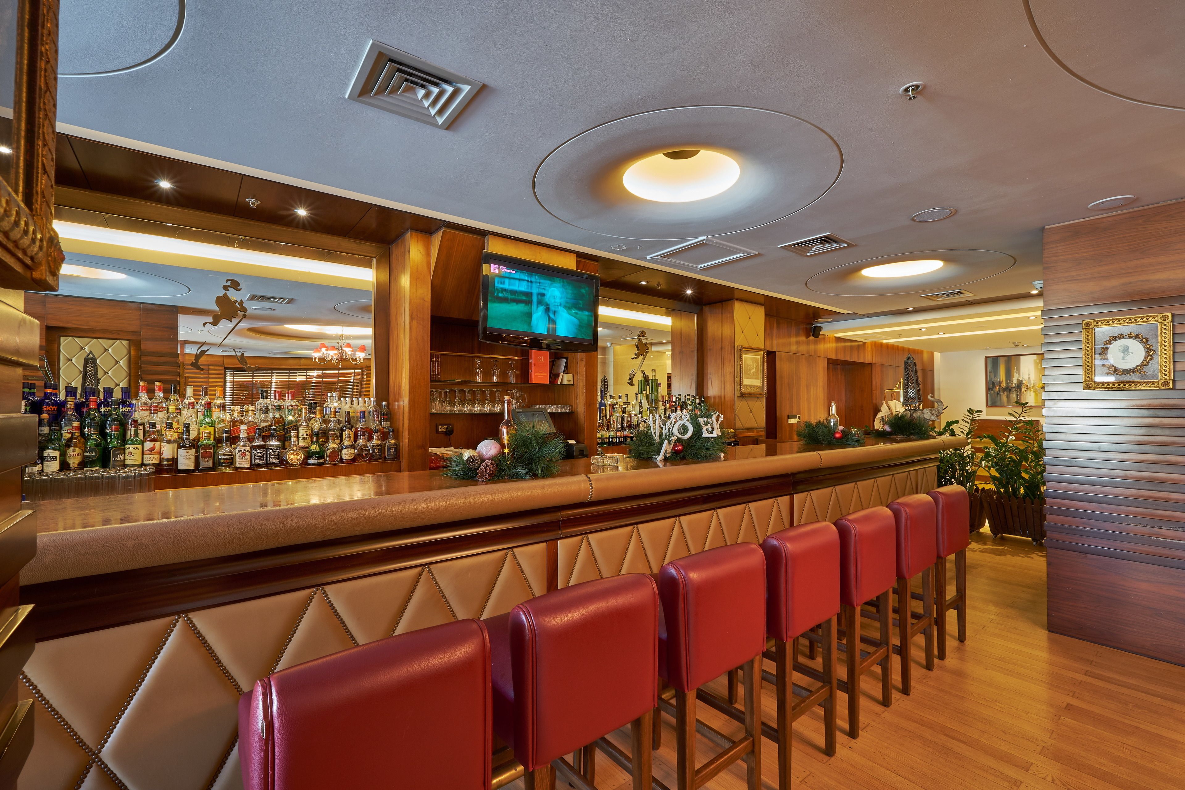 A bar area with a long counter, multiple stools, and a television screen.
