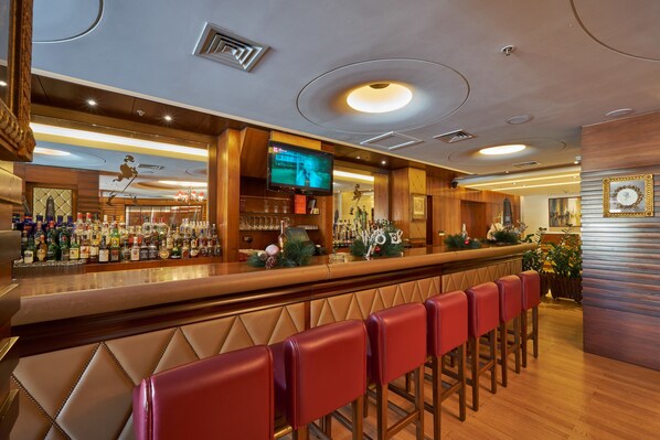 A bar area with a long counter, multiple stools, and a television screen. - Coral Beach Hotel and Resort Beirut (Ghobeiry)