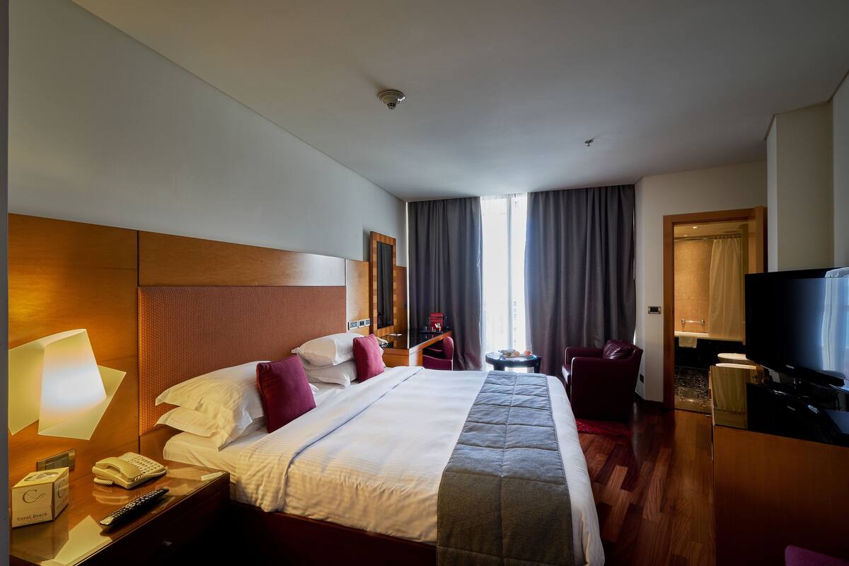 Une chambre d’hôtel avec un grand lit, une télévision, un bureau avec une lampe, un téléphone et une petite table avec une télécommande.