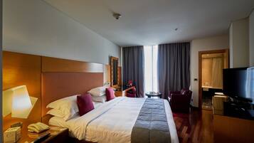 Habitación de hotel con una cama grande, un televisor, un escritorio con lámpara, un teléfono y una mesita con control remoto.
