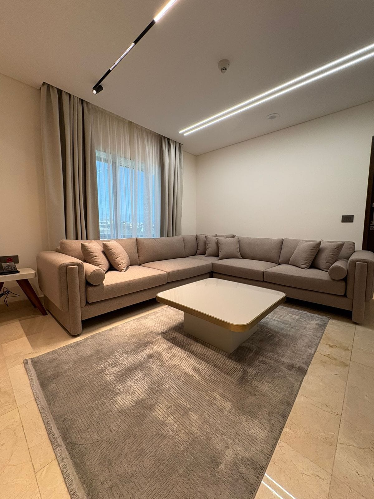 Una sala moderna con un sofá modular, una mesa de centro y un ventanal con cortinas.