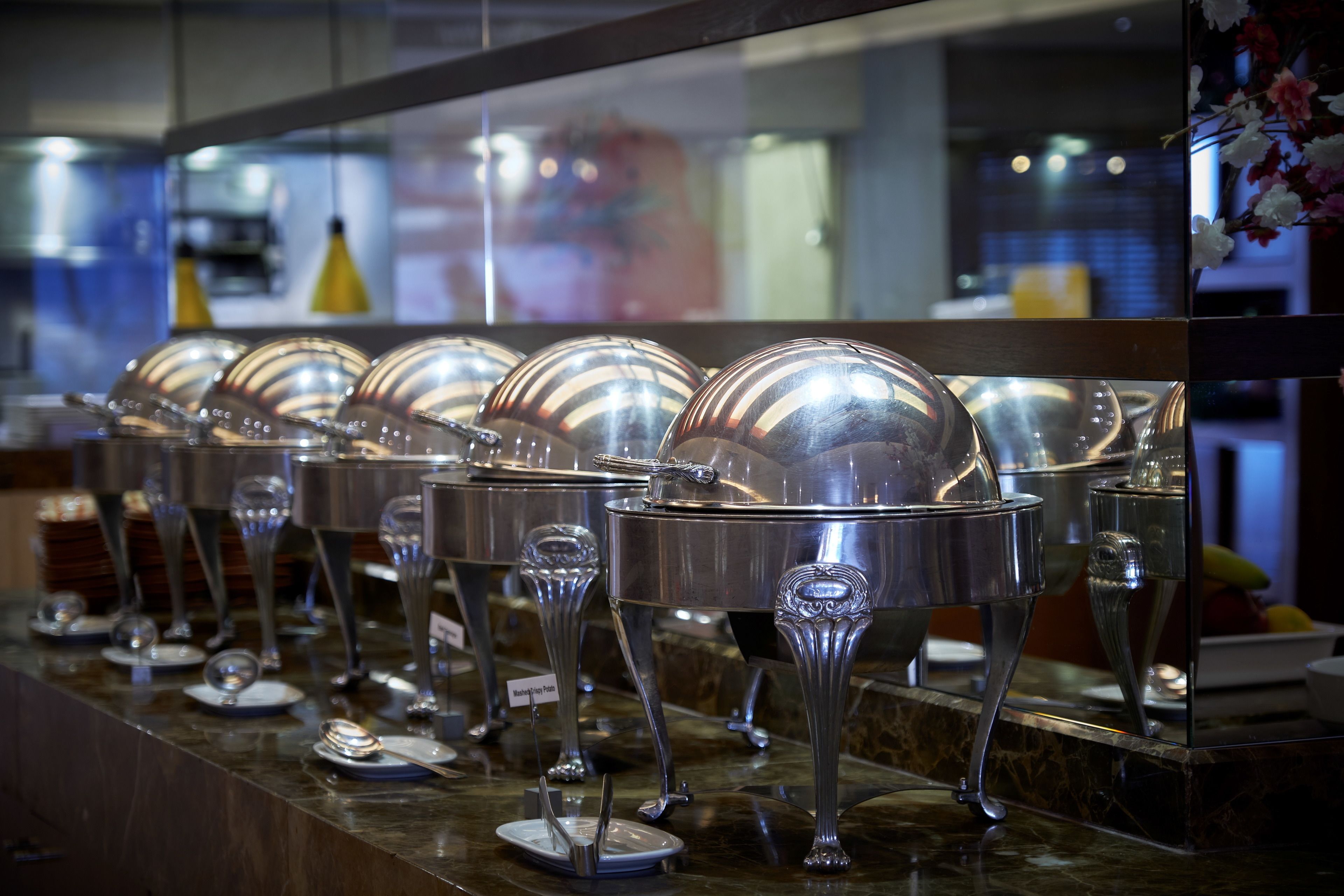 Una mesa de buffet con varias estaciones de servicio, cada una con un bol de metal y una cuchara.
