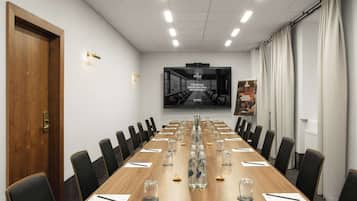 A conference room with a long wooden table, black chairs, and a large screen displaying a professional memorial advertisement.