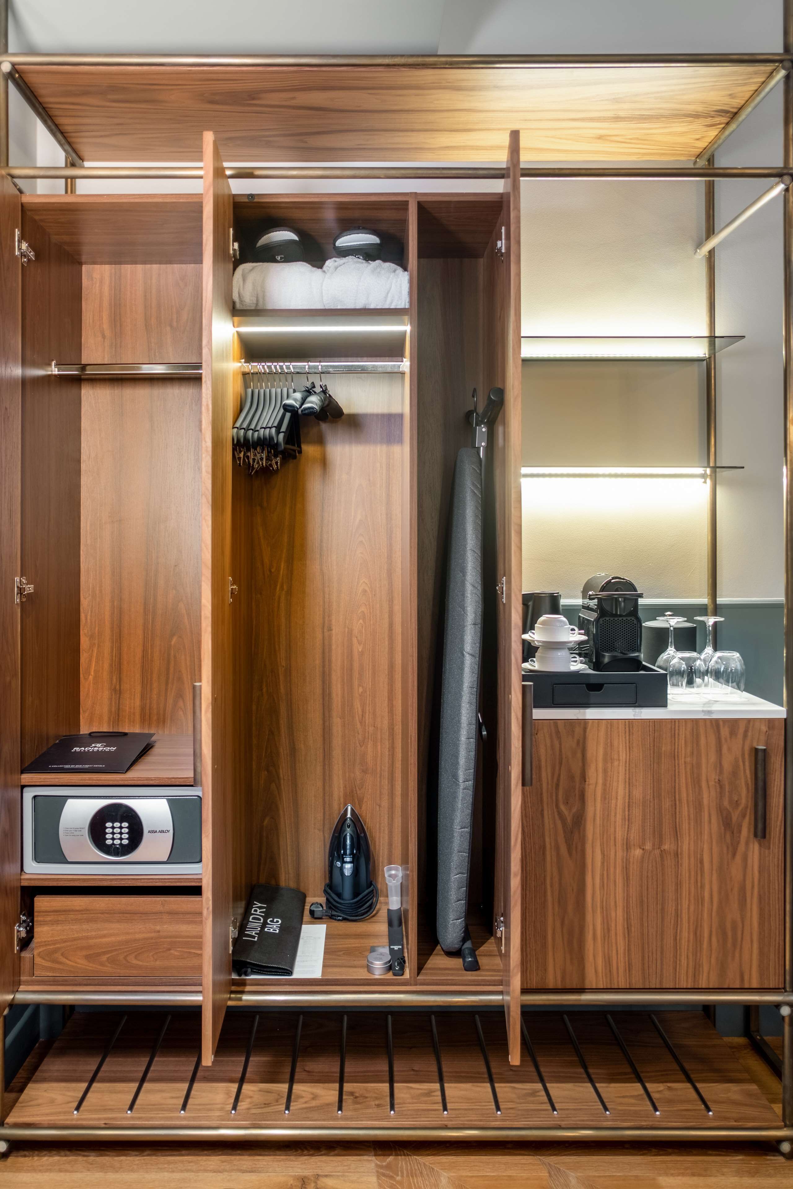 A hotel room with a wooden wardrobe, a minibar, and a small seating area with a table and chairs.