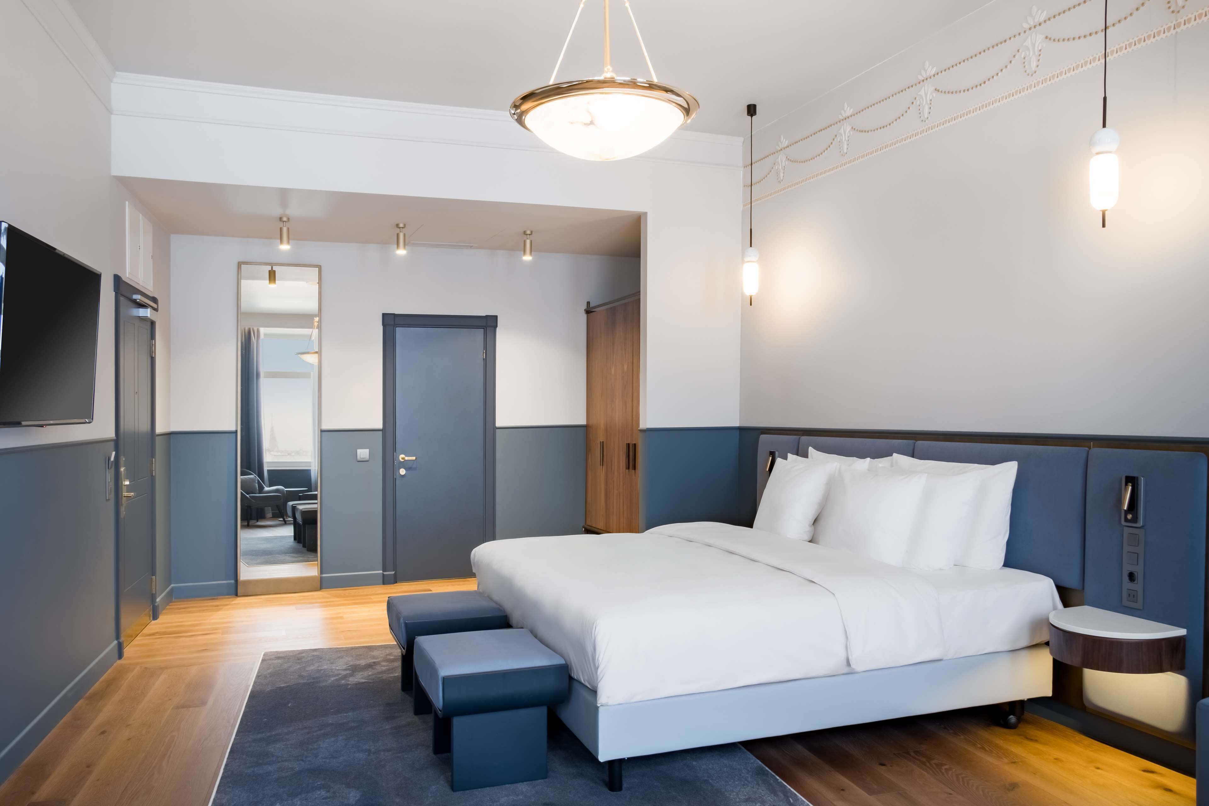 A modern hotel room with a large bed, a TV, a wooden wardrobe, and a small bedside table.