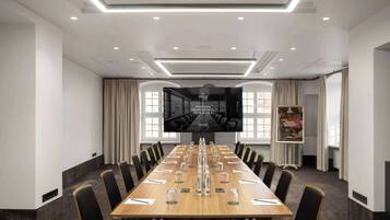 A conference room with a long table, chairs, a large screen, and a poster.