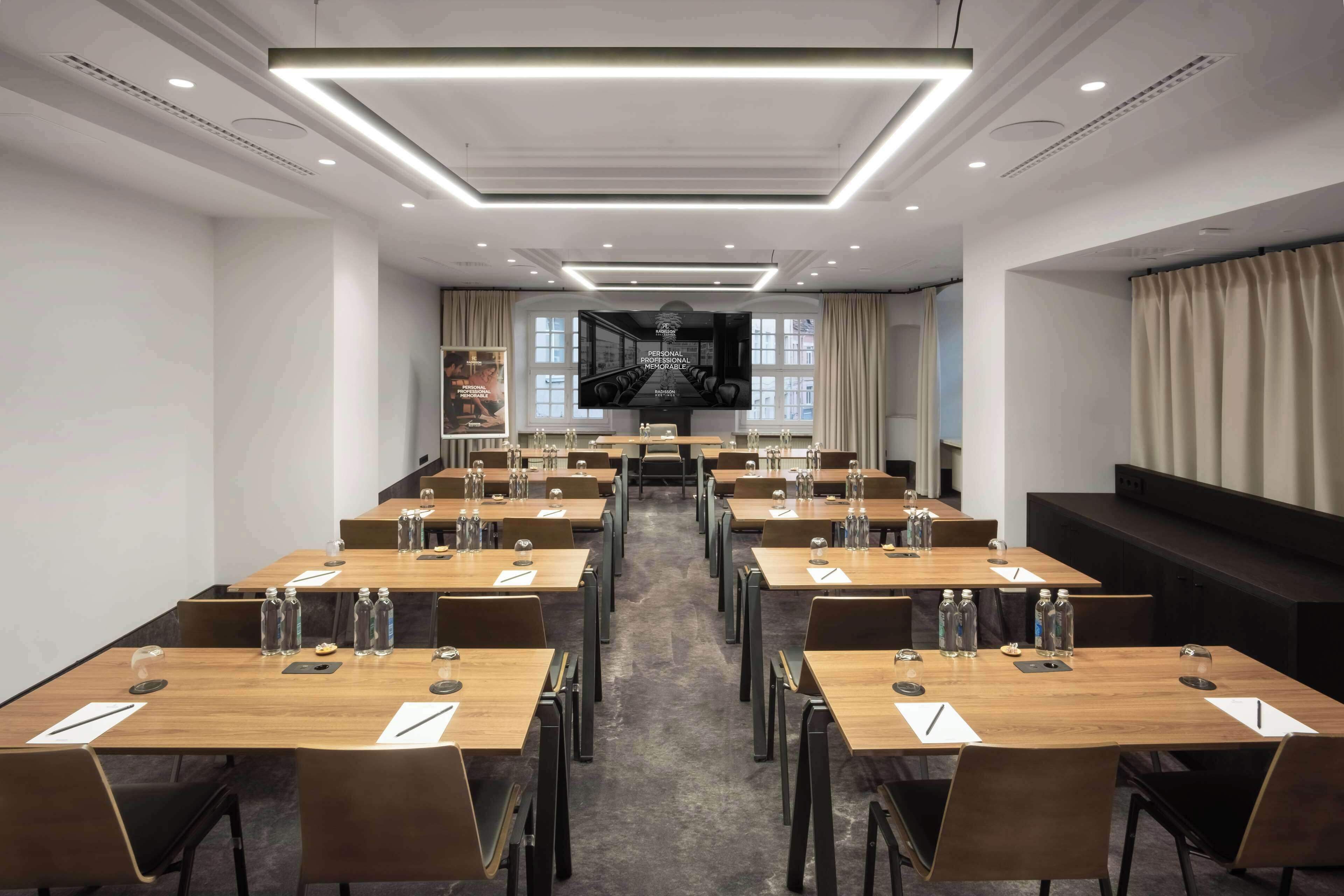 A conference room with multiple tables, chairs, and a large screen at the front.