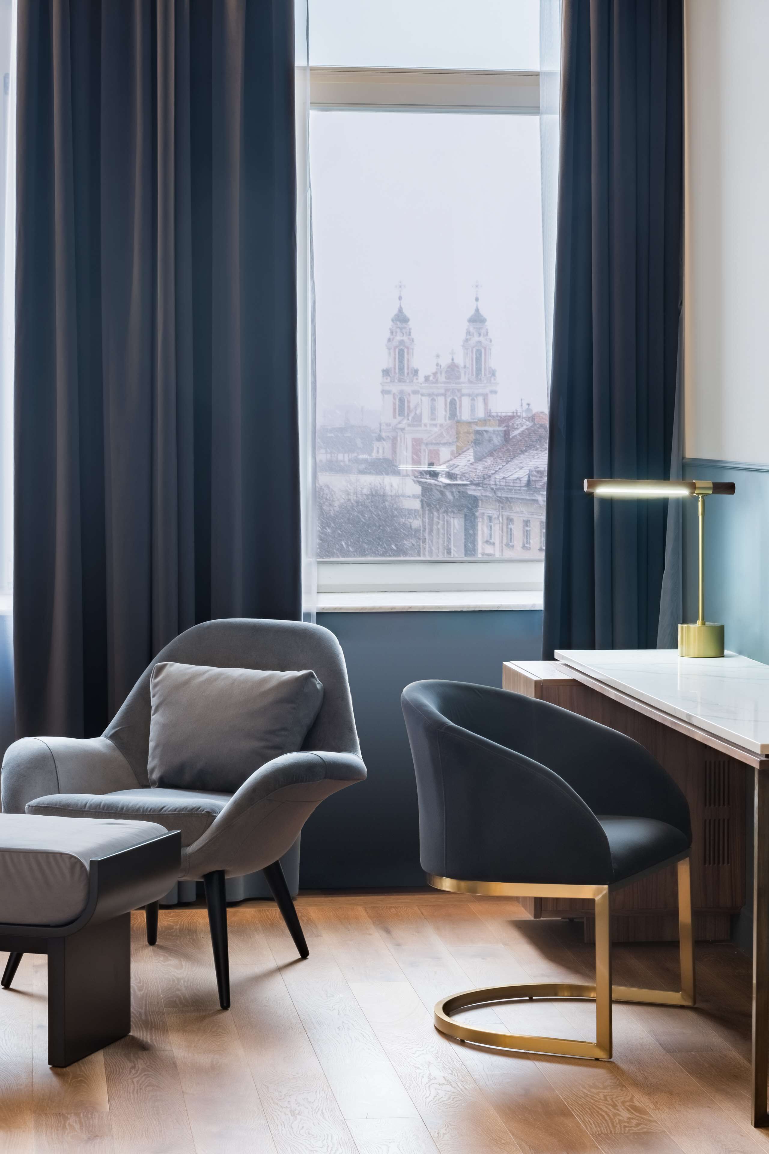 Une chambre moderne avec vue sur un bâtiment historique, un bureau avec une lampe et deux chaises.