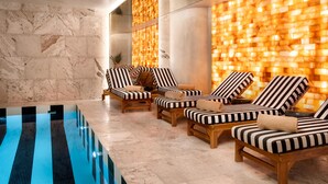 Un área al lado de la piscina con sillones de descanso, suelo de baldosas y una pared con diseño texturizado.