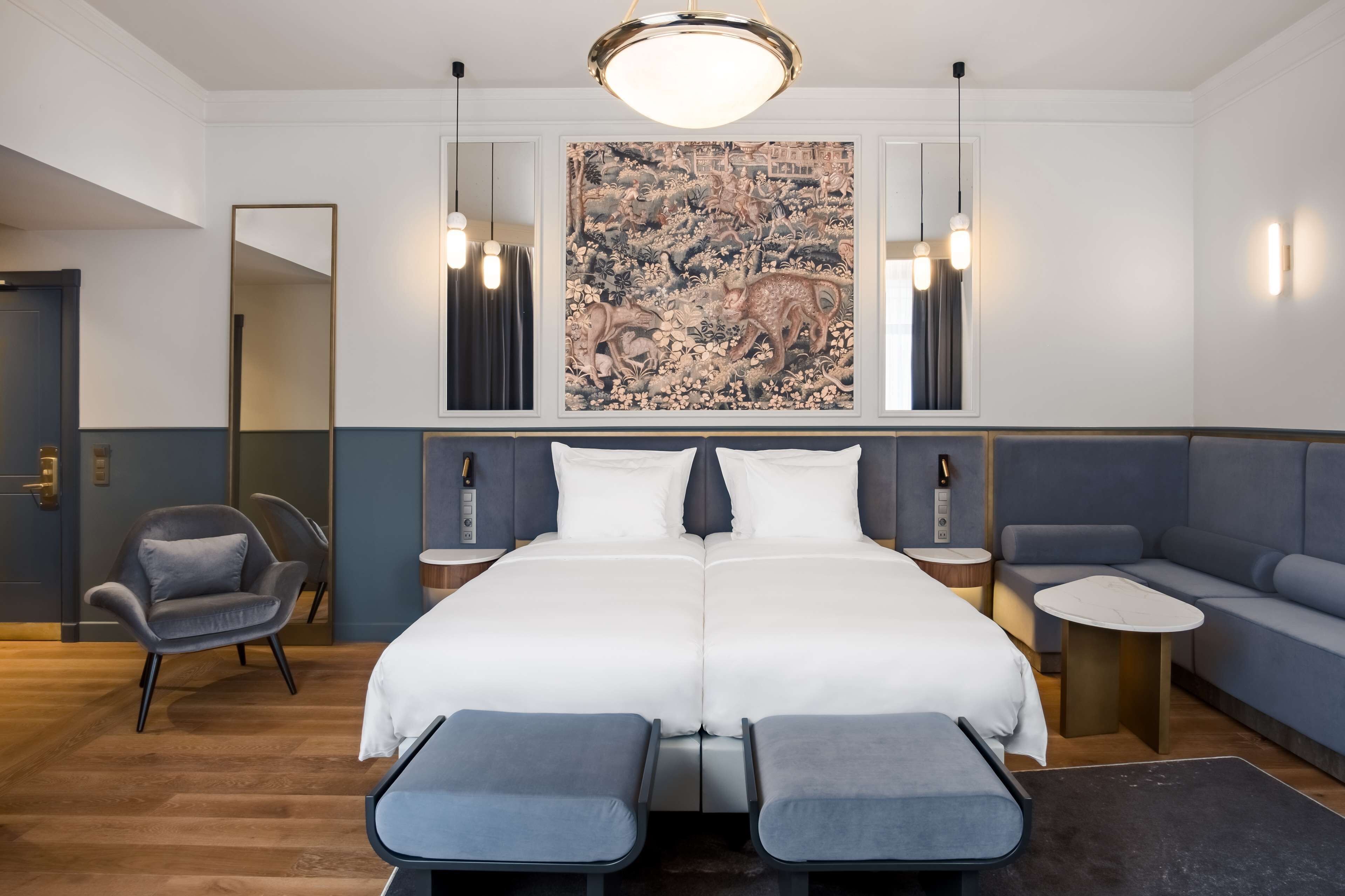 A modern hotel room with a large bed, a seating area, and a large painting on the wall.