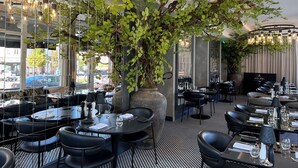 Un restaurante con mesas redondas, sillas negras y lámparas colgantes.