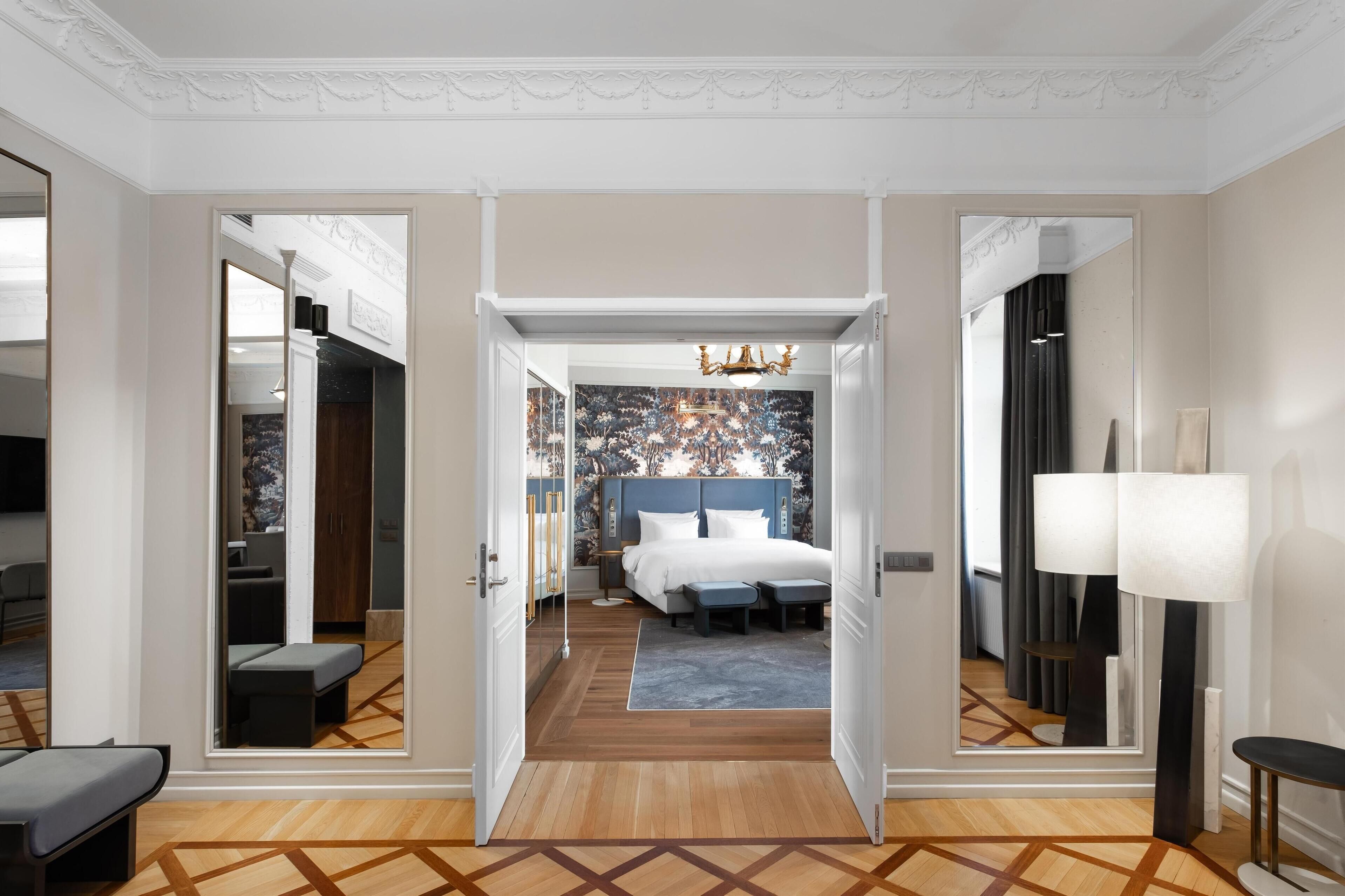 Una habitación de hotel con una cama grande, una zona de estar con un banco, un espejo y una lámpara.