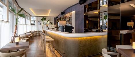 A modern bar area with a curved counter, wooden flooring, and white chairs.