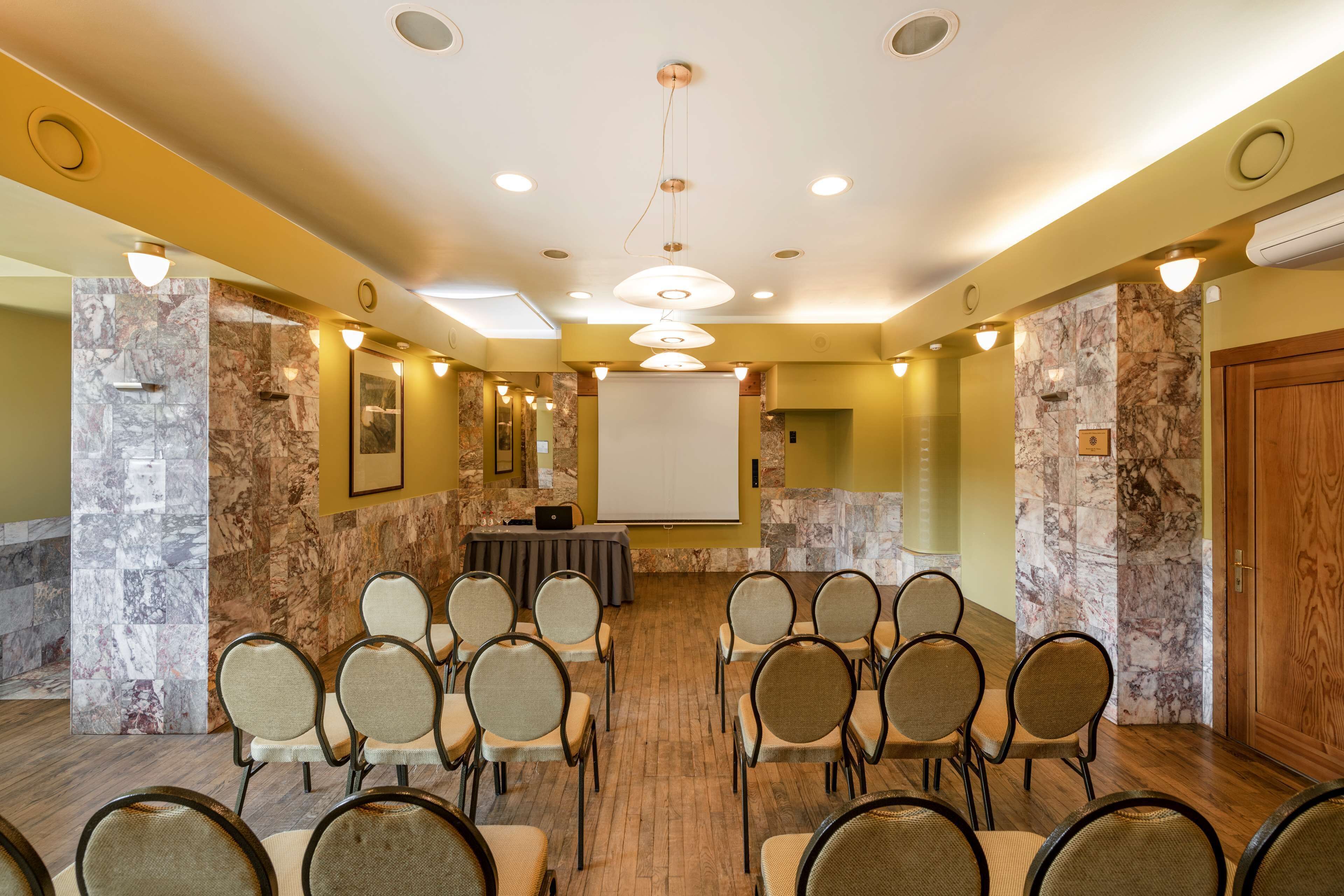 A conference room with a marble wall, a projector screen, and a laptop on a table.