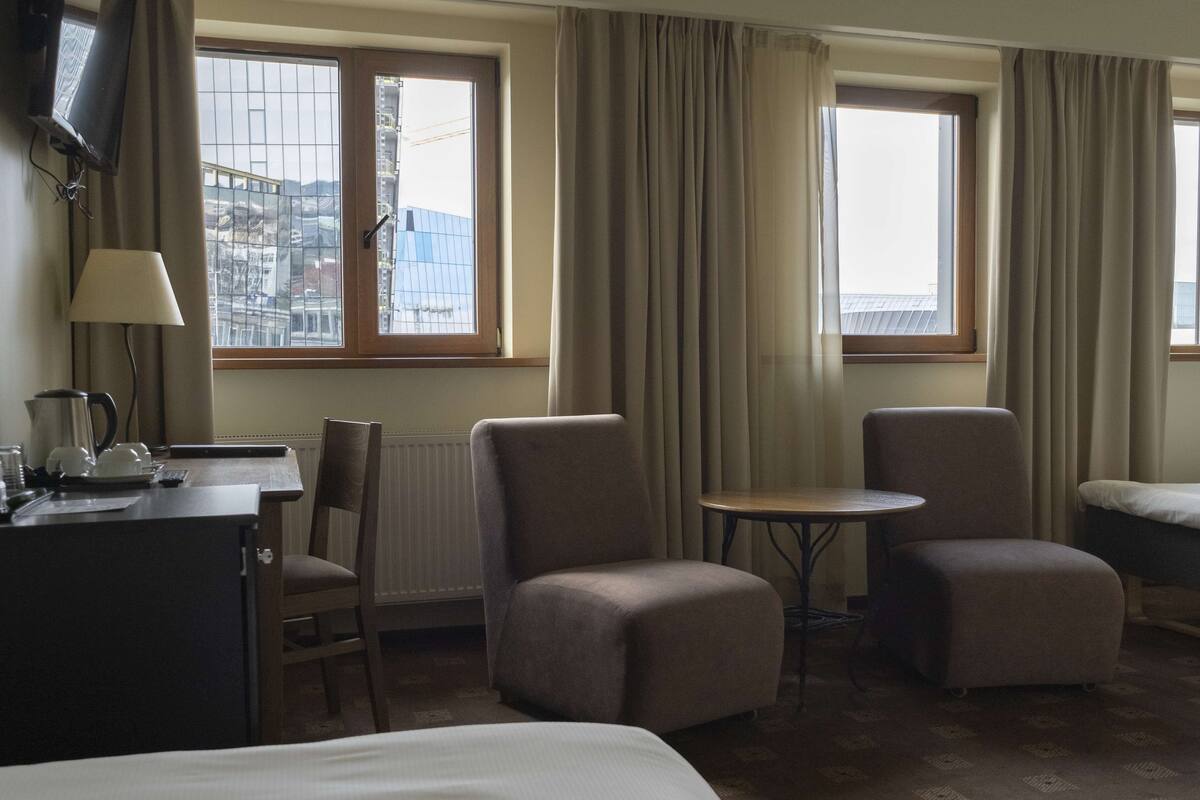 A hotel room with a bed, two armchairs, a small table, a desk with a lamp, and a TV.