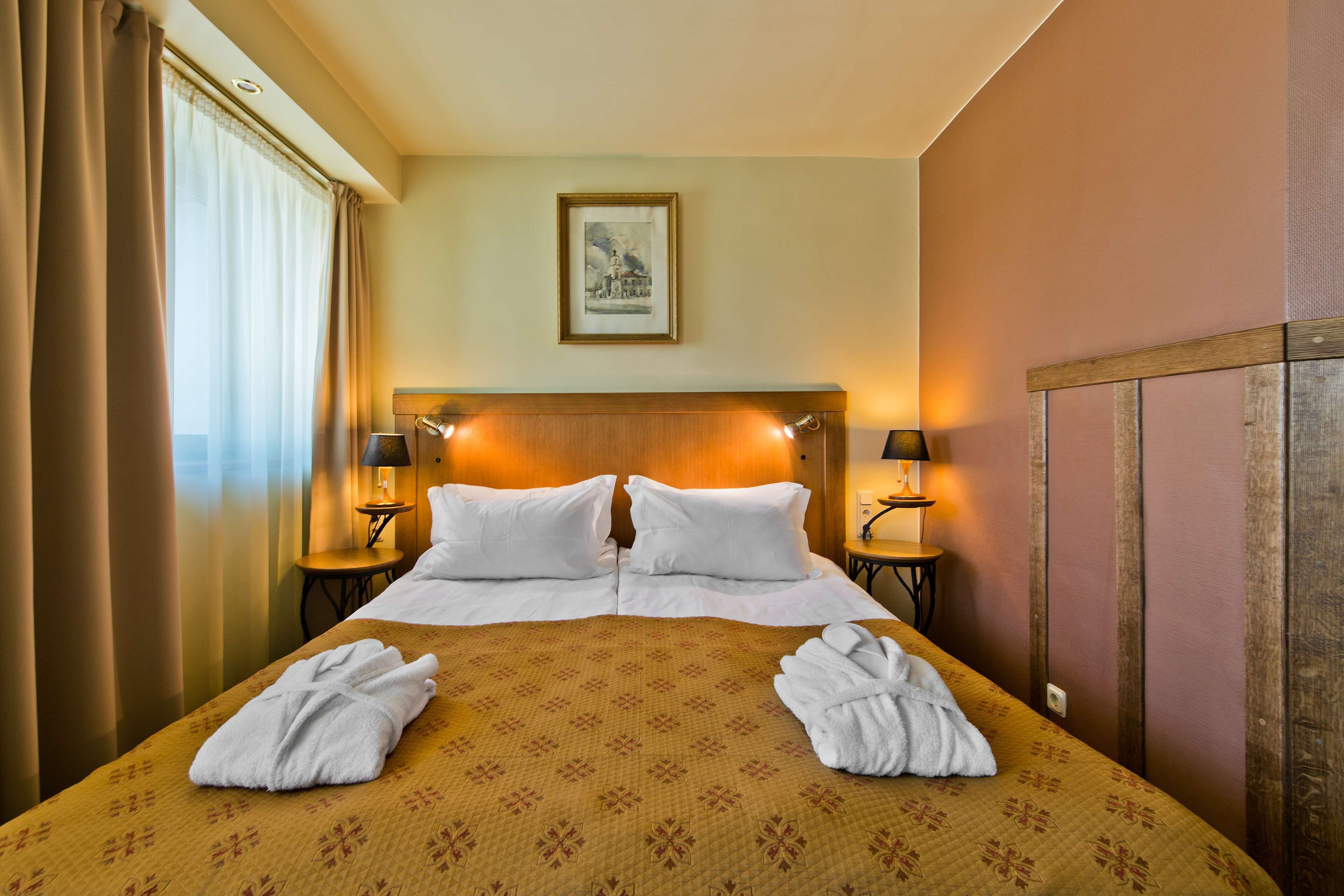 A hotel room with a large bed, two bedside tables with lamps, a framed picture on the wall, and two towels on the bed.