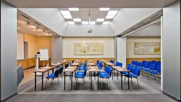 Uma sala de conferências com mesas, cadeiras, um projetor e duas pinturas nas paredes.