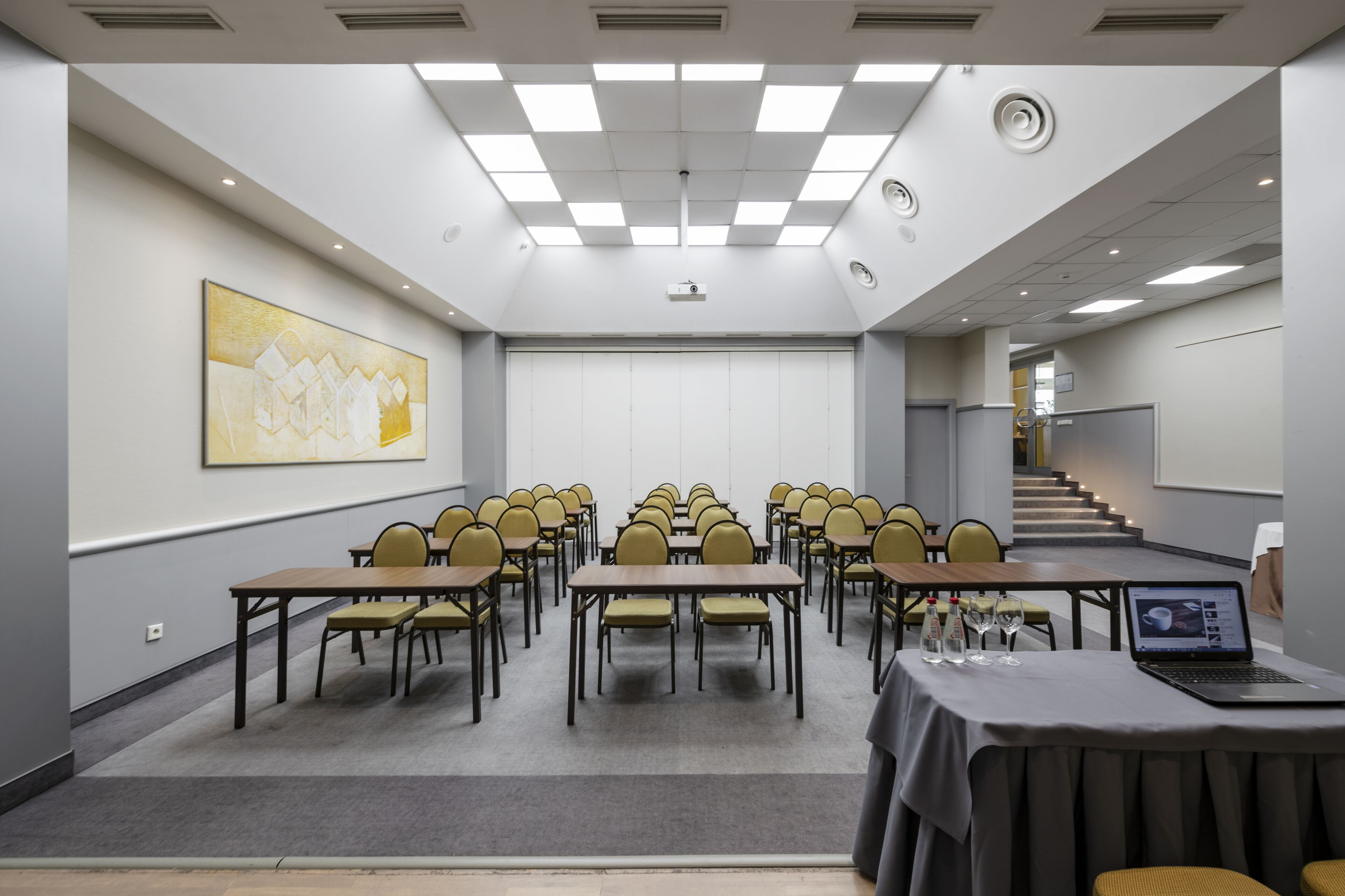 A conference room with tables and chairs, a projector, and a laptop on a table.