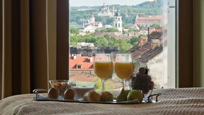 A breakfast tray with eggs, bread, and juice glasses, and a view of a cityscape with buildings and a hill in the background. - Best Western Vilnius (Vilnius)