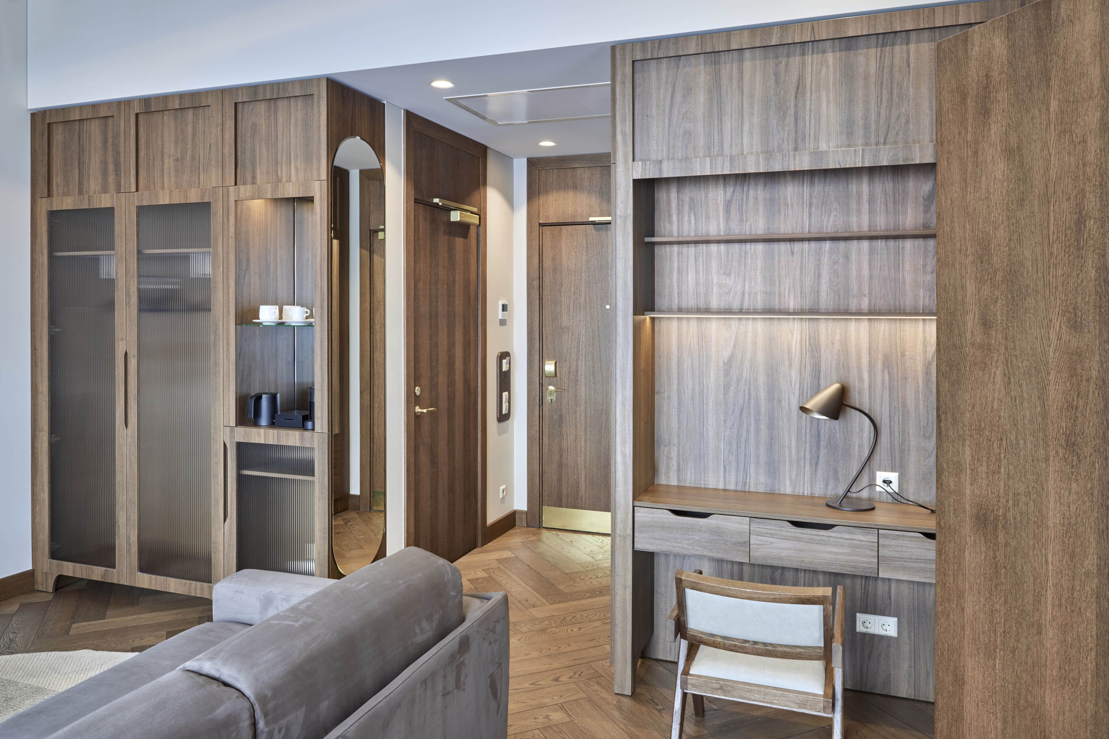 A modern bedroom with a wooden wardrobe, a desk with a chair, and a large mirror.