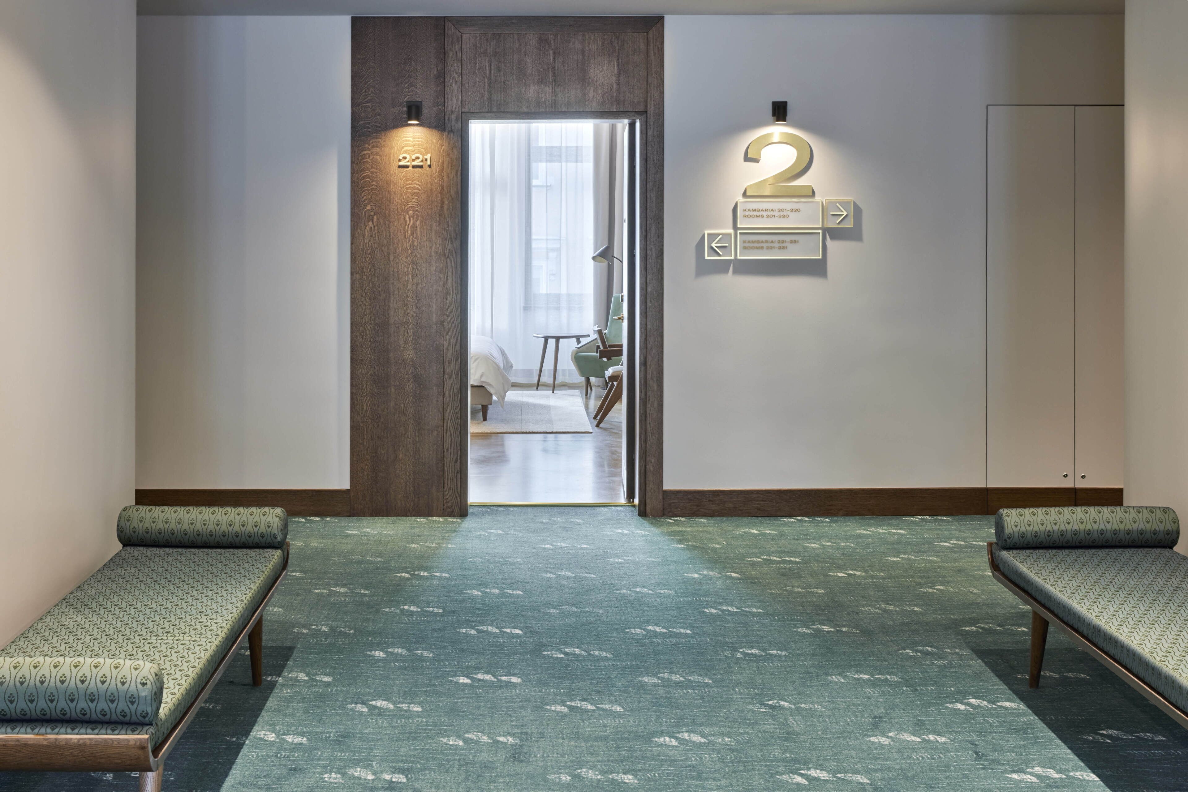 Vestíbulo de hotel con mostrador de recepción, cartel con el número 221, indicaciones y dos zonas de estar.