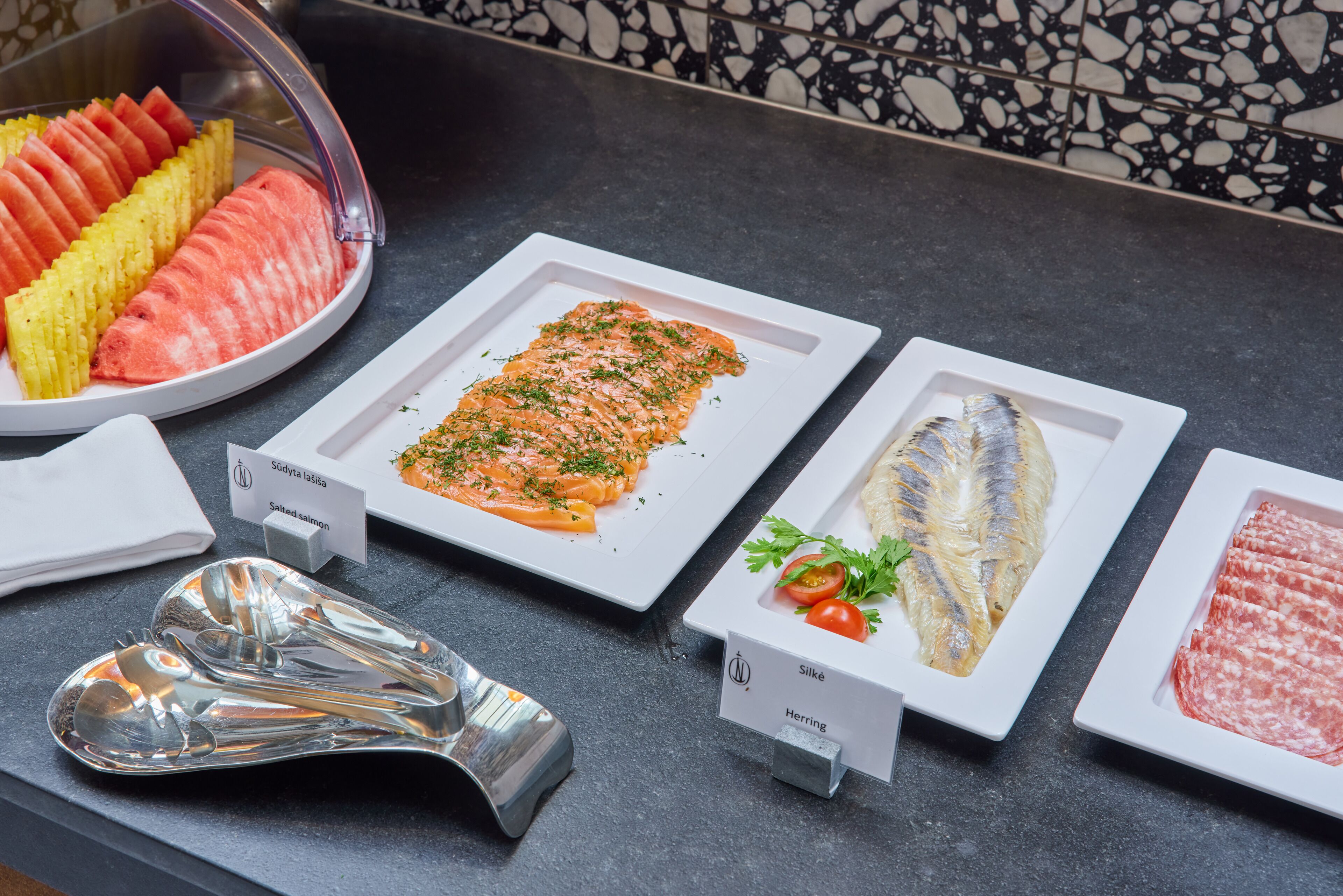 A buffet with various food options including salmon, herring, and silke, along with a selection of fruits.