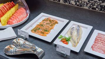 A buffet with various food options including salmon, herring, and silke, along with a selection of fruits.